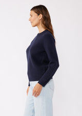 [Color: Navy] A brunette model wearing a classic crew neck sweater in navy blue. With ribbed trims, long sleeves, and a cable knit stitch detail. A versatile sweater perfect for layering during colder temperatures or wearing on its own. 