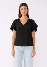 [Color: Black] A brunette model wearing a sophisticated black top. With double short flutter sleeves, smocked neck detail, split v neck, and a relaxed fit. An everyday top perfect for the office or a casual outing.