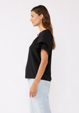 [Color: Black] A brunette model wearing a sophisticated black top. With double short flutter sleeves, smocked neck detail, split v neck, and a relaxed fit. An everyday top perfect for the office or a casual outing.