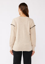 [Color: Oatmeal] A brunette model wearing an everyday sweater with a relaxed silhouette in a beige tan. With a classic v neckline, long sleeves, and an exposed seam with blanket stitch. A fall sweater styled with black bottom and casual sandals. 