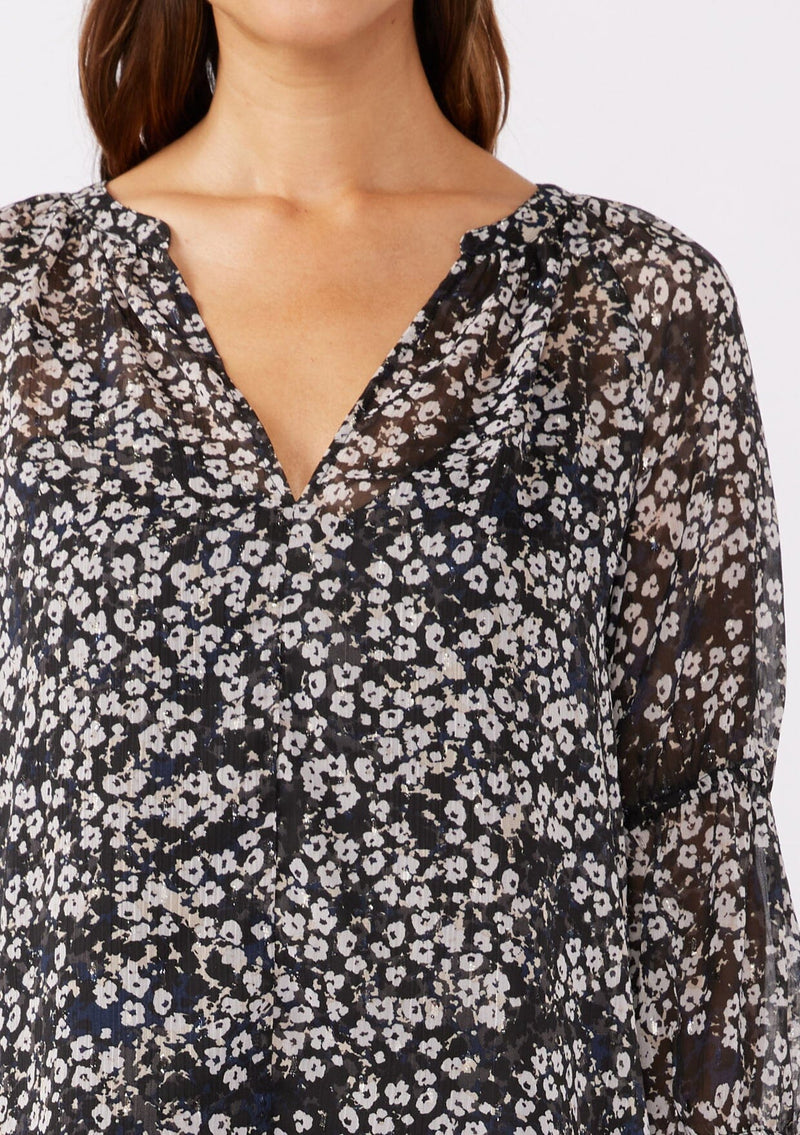 [Color: Black/Grey] A brunette woman wearing an ultra flowy chiffon blouse with metallic clip dot details. A black floral blouse with a split v neckline, long sleeves, and elastic cuffs. Paired with denim jeans for a relaxed fall look, perfect for dinner and classy evening parties.