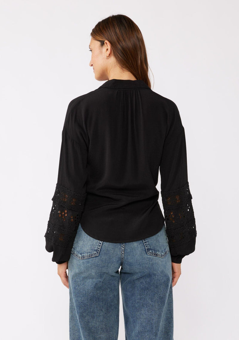 [Color: Black] A back image of a brunette model wearing a sexy black tie front top with embroidered and lace trim details. A casual, everyday black top with a collared neckline, long sleeves, and an elastic wrist cuff. 