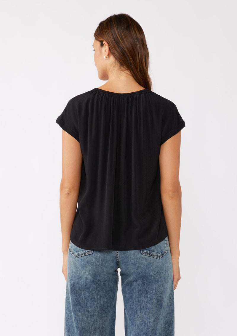 [Color: Black] A brunette model wearing a relaxed fit black top. With self neck ties, ruched split v neckline, and short dolman sleeves. Styled with a cute denim bottoms for a laid back look.