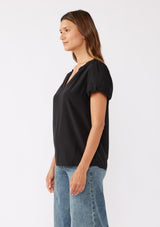 [Color: Black] A brunette model wearing a sophisticated classic black top with denim jeans. Featuring bubble puff sleeves, ruffled neckline, and a tie neck detail. A relaxed fit top perfect for the office or as a formal attire.