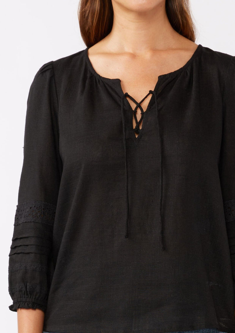 [Color: Black] A brunette model wearing a bohemian black blouse with embroidered lace details. Crafted from a rayon and linen blend, this top feature long sleeves, a lace up front, and elastic cuffs. Perfect addition to any fall bohemian wardrobe.  