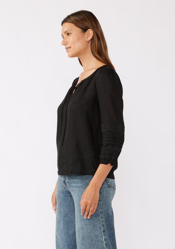 [Color: Black] A brunette model wearing a bohemian black blouse with embroidered lace details. Crafted from a rayon and linen blend, this top feature long sleeves, a lace up front, and elastic cuffs. Perfect addition to any fall bohemian wardrobe.  