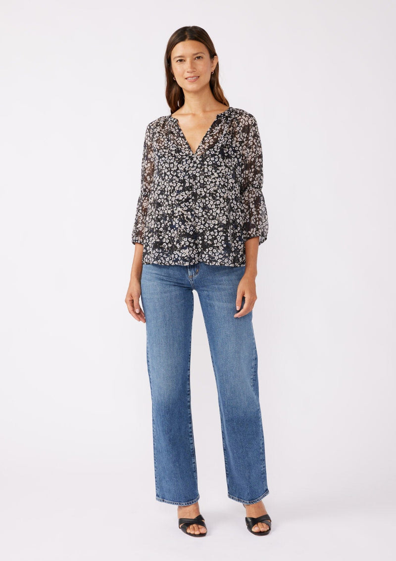 [Color: Black/Grey] A brunette woman wearing an ultra flowy chiffon blouse with metallic clip dot details. A black floral blouse with a split v neckline, long sleeves, and elastic cuffs. Paired with denim jeans for a relaxed fall look, perfect for dinner and classy evening parties.