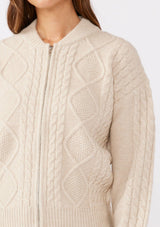 [Color: Natural] A brunette model wearing an off white, ivory cozy knit sweater with a zipper front. Featuring long sleeves and classic ribbed trims. A versatile sweater perfect for layering and styling any fall ensemble. 