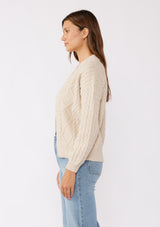 [Color: Natural] A brunette model wearing an off white, ivory cozy knit sweater with a zipper front. Featuring long sleeves and classic ribbed trims. A versatile sweater perfect for layering and styling any fall ensemble. 