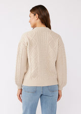 [Color: Natural] A brunette model wearing an off white, ivory cozy knit sweater with a zipper front. Featuring long sleeves and classic ribbed trims. A versatile sweater perfect for layering and styling any fall ensemble. 