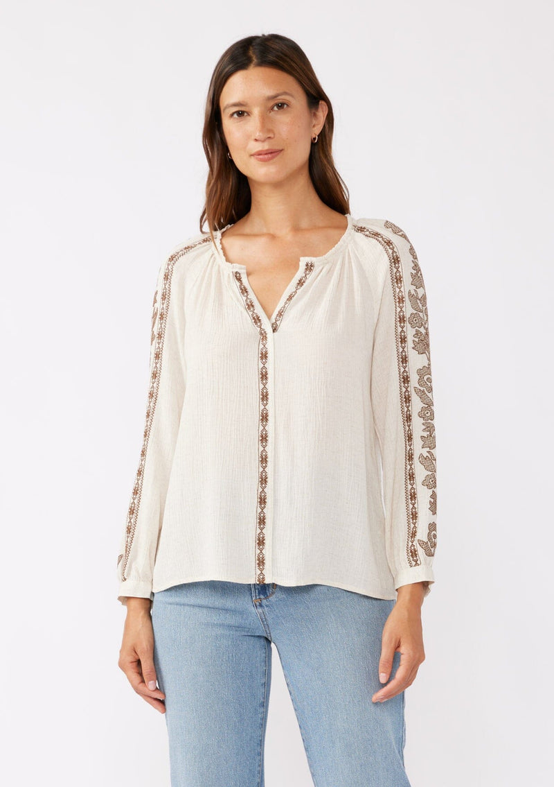 [Color: Natural/Mocha] A brunette model wearing an ultra bohemian blouse in off white with brown embroidery. Featuring a split v neckline, long sleeves, and a relaxed fit.