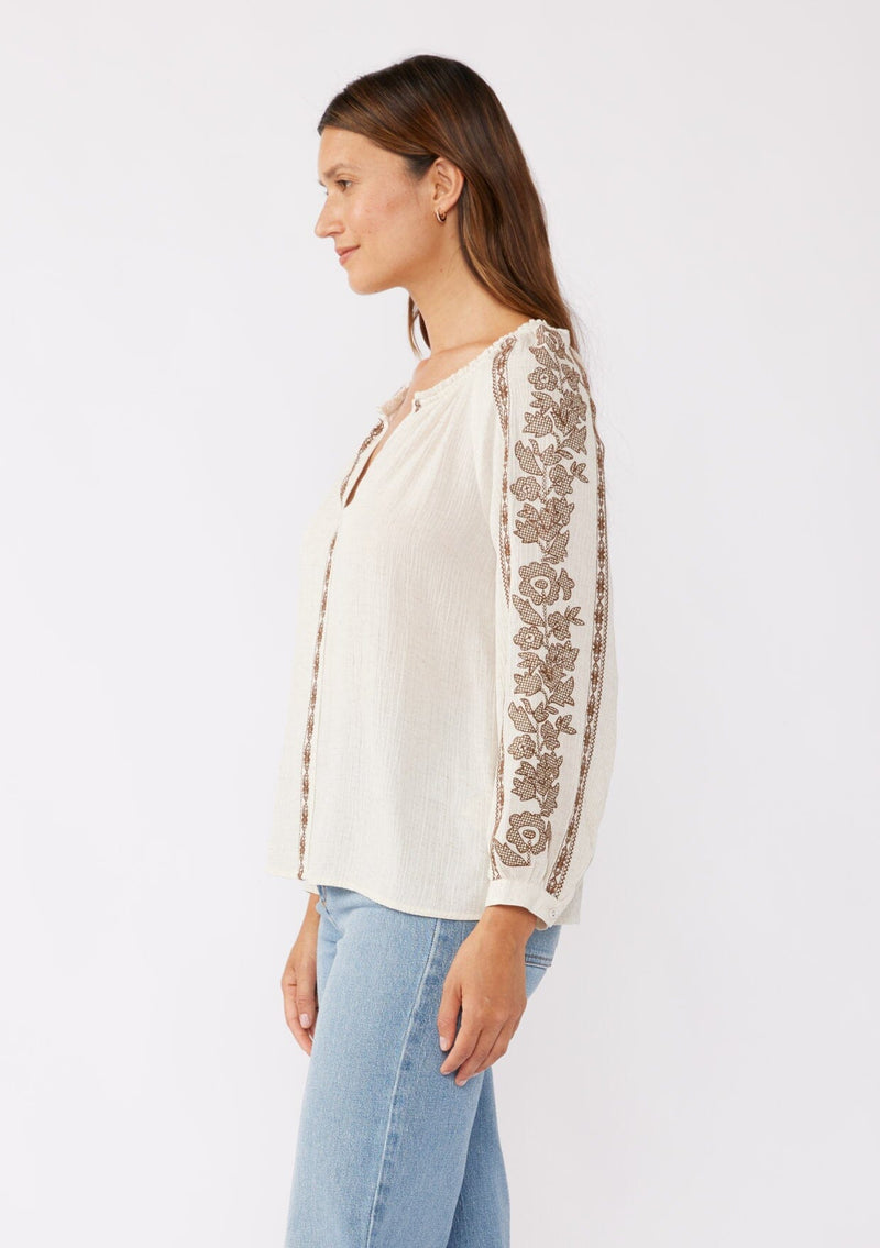 [Color: Natural/Mocha] A brunette model wearing an ultra bohemian blouse in off white with brown embroidery. Featuring a split v neckline, long sleeves, and a relaxed fit.