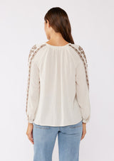 [Color: Natural/Mocha] A brunette model wearing an ultra bohemian blouse in off white with brown embroidery. Featuring a split v neckline, long sleeves, and a relaxed fit.