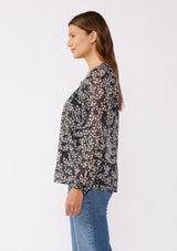 [Color: Black/Grey] A brunette model wearing a relaxed fit blouse in black and ivory floral print with shimmering metallic clip dot details. A classic, timeless blouse in a flowy chiffon with long sleeves and a button front. Perfect for the office or late night dinners.  