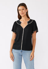 [Color: Black/Natural] A brunette model wearing a classic bohemian top in black. With an embroidered blanket stitch trim, short flutter sleeves, and a split v neckline. Perfect for any fall wardrobe; styled with denim for a cool and casual look.  