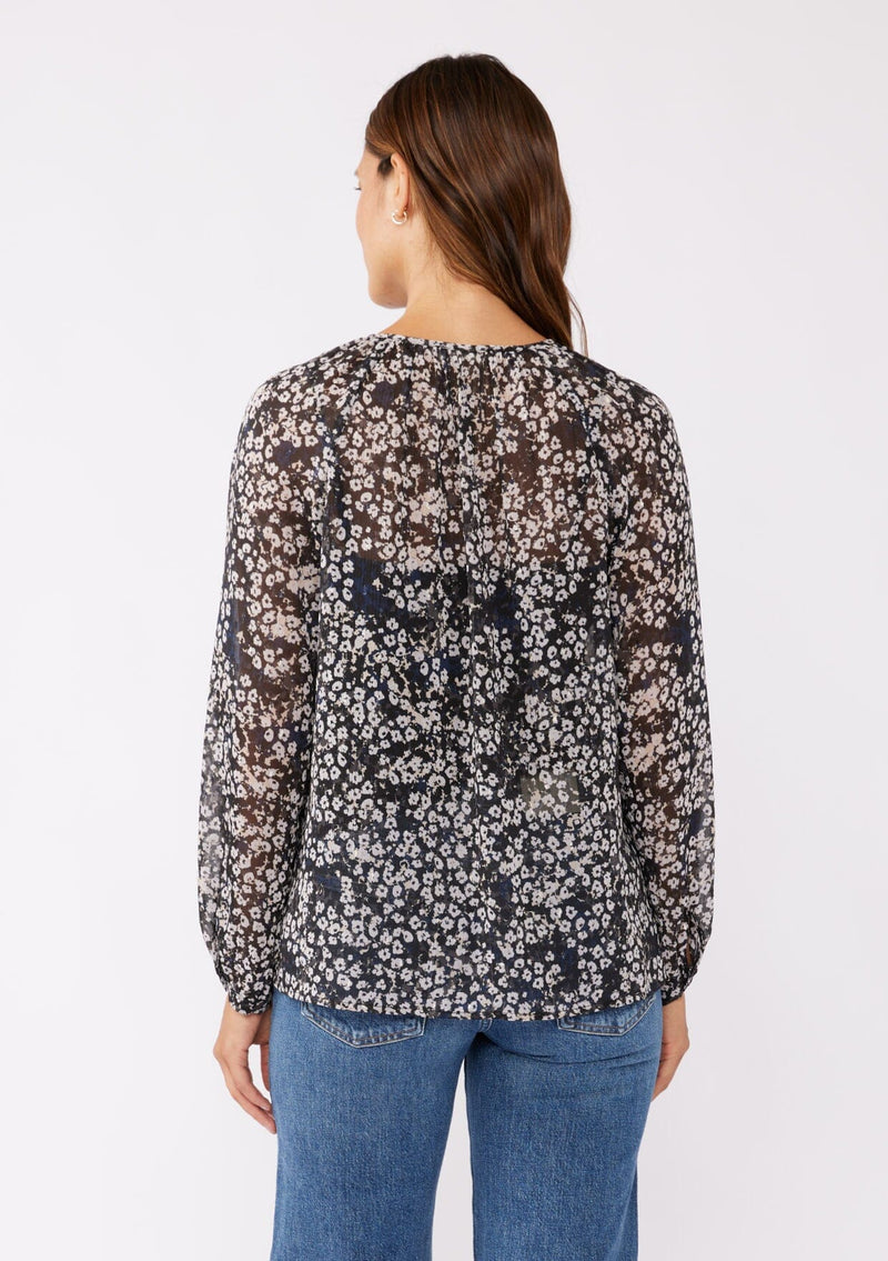 [Color: Black/Grey] A brunette model wearing a relaxed fit blouse in black and ivory floral print with shimmering metallic clip dot details. A classic, timeless blouse in a flowy chiffon with long sleeves and a button front. Perfect for the office or late night dinners.  