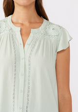 [Color: Mint] A brunette model wearing a classic Lovestitch button up top in green mint. With short flutter sleeves, split v neckline, and a floral lace trim at the yoke. Perfect for the summer and beyond.