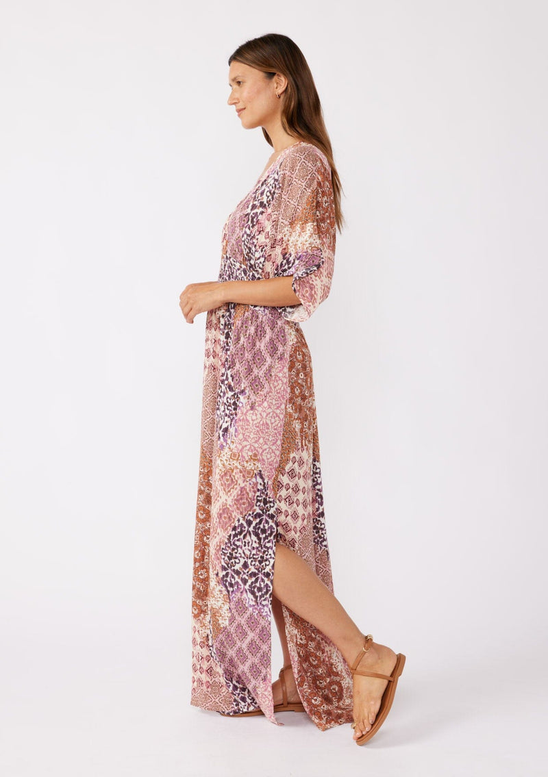 [Color: Natural/Clay] A blonde model wearing an ultra bohemian maxi dress in a pink patchwork print. Featuring flowy kimono sleeves, v neckline, smocked waist, a sexy open back with tie detail, and side slits. Perfect as a beach cover up or casual outings. 