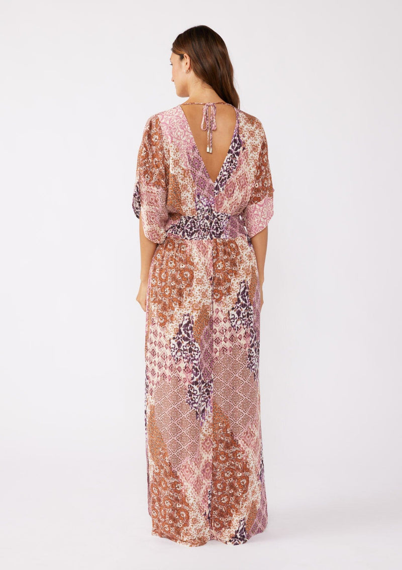 [Color: Natural/Clay] A blonde model wearing an ultra bohemian maxi dress in a pink patchwork print. Featuring flowy kimono sleeves, v neckline, smocked waist, a sexy open back with tie detail, and side slits. Perfect as a beach cover up or casual outings. 