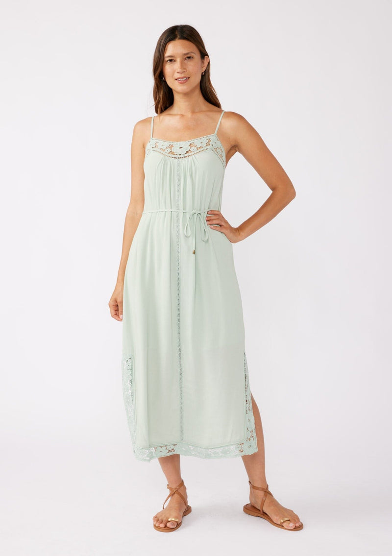 [Color: Mint] A brunette model wearing a mint green midi dress with a floral lace trim. A casual dress with adjustable spaghetti straps, scoop neckline, tie waist detail, and side slits. An ultra flowy midi dress for the summer and beyond. 