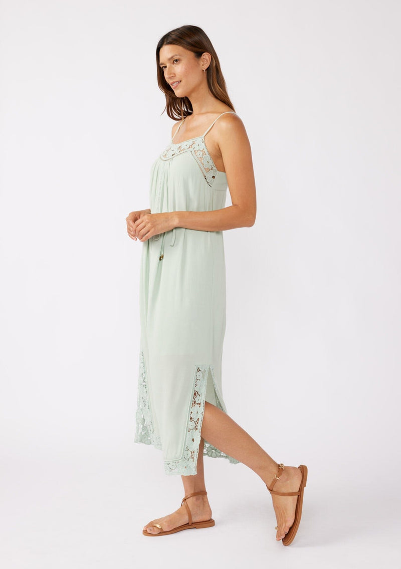 [Color: Mint] A brunette model wearing a mint green midi dress with a floral lace trim. A casual dress with adjustable spaghetti straps, scoop neckline, tie waist detail, and side slits. An ultra flowy midi dress for the summer and beyond.