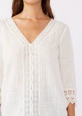 [Color: Vanilla] A blonde model wearing a textured cotton blouse in ivory white. With lace and crochet trims, functional button front, v neckline, and relaxed fit. A casual bohemian top paired with denim jeans.