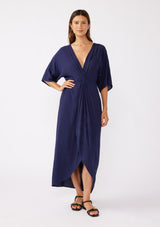 [Color: Navy/Navy] A brunette model wearing a blue front knot maxi dress with a tonal embroidery. Featuring a deep v neckline, kimono sleeves, front slit, and an asymmetrical hem. A bohemian style maxi dress with a relaxed fit.