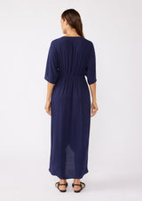 [Color: Navy/Navy] A brunette model wearing a blue front knot maxi dress with a tonal embroidery. Featuring a deep v neckline, kimono sleeves, front slit, and an asymmetrical hem. A bohemian style maxi dress with a relaxed fit.