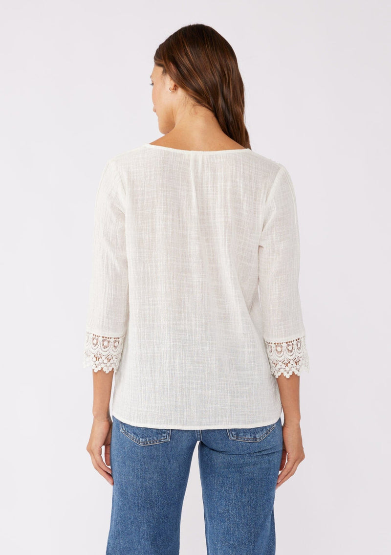 [Color: Vanilla] A blonde model wearing a textured cotton blouse in ivory white. With lace and crochet trims, functional button front, v neckline, and relaxed fit. A casual bohemian top paired with denim jeans.