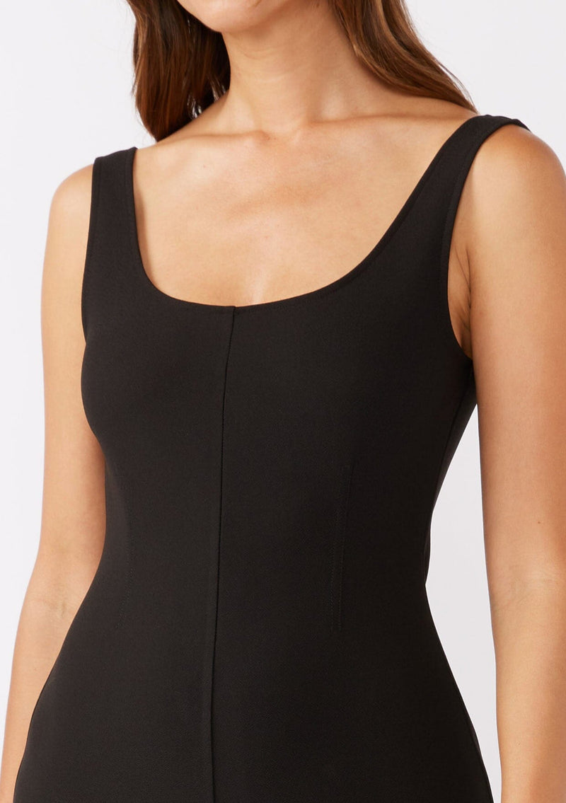 [Color: Black] A brunette model wearing an all black jumpsuit with a slim fit bodice and wide legs. Featuring a flattering scoop neckline and back and thick tank top straps. Paired casually with thick strappy sandals for a casual look. An ideal jumpsuit for sophisticated events or office.