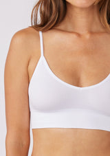 [Color: White] A brunette model wearing a fitted crop lingerie top in white. A casual yet stylish undergarment perfect for styling under dresses or wearing on it's own as a sports bra. A comfortable stretchy ribbed knit top with a low back and spaghetti straps.