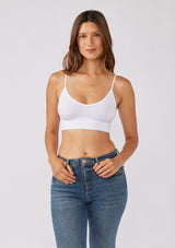 [Color: White] A brunette model wearing a fitted crop lingerie top in white. A casual yet stylish undergarment perfect for styling under dresses or wearing on it's own as a sports bra. A comfortable stretchy ribbed knit top with a low back and spaghetti straps.