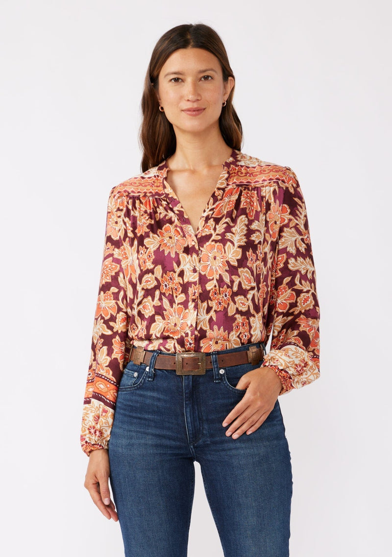 [Color: Wine/Dusty Rose] A front image of a brunette model wearing an orange and red floral print blouse with a functional button front. With a relaxed fit, split v neckline, long sleeves, and elastic cuffs. 