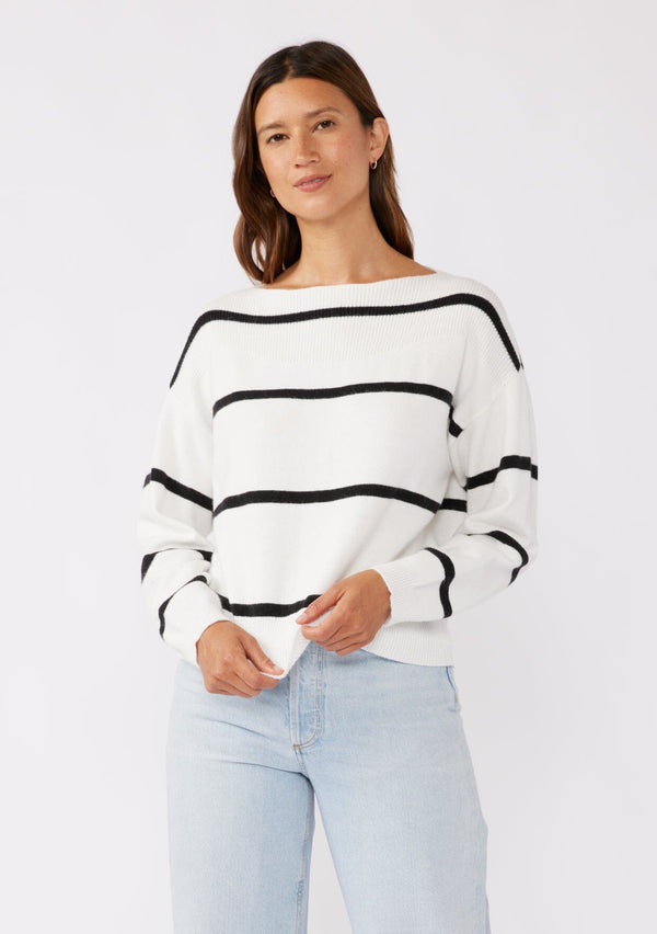 [Color: White/Black] A brunette model wearing a classic black and white striped knit pullover sweater. With long sleeves, a boat neckline, and ribbed trims. Perfectly relaxed and boxy for everyday styling. 