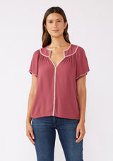 [Color: Mauve/Natural] A brunette model wearing a classic bohemian top in a mauve pink hue. With an embroidered blanket stitch trim, short flutter sleeves, and a split v neckline. Perfect for any fall wardrobe; styled with denim for a cool and casual look.  