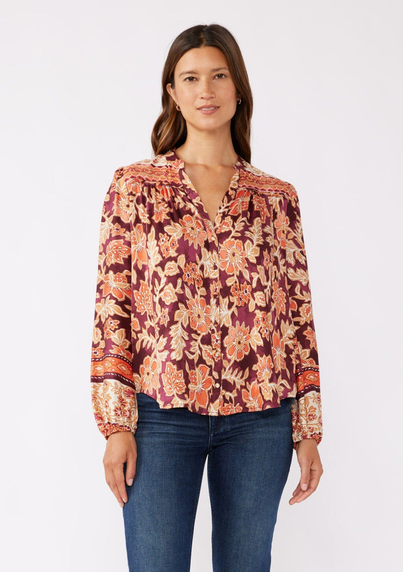 [Color: Wine/Dusty Rose] A front image of a brunette model wearing an orange and red floral print blouse with a functional button front. With a relaxed fit, split v neckline, long sleeves, and elastic cuffs. 