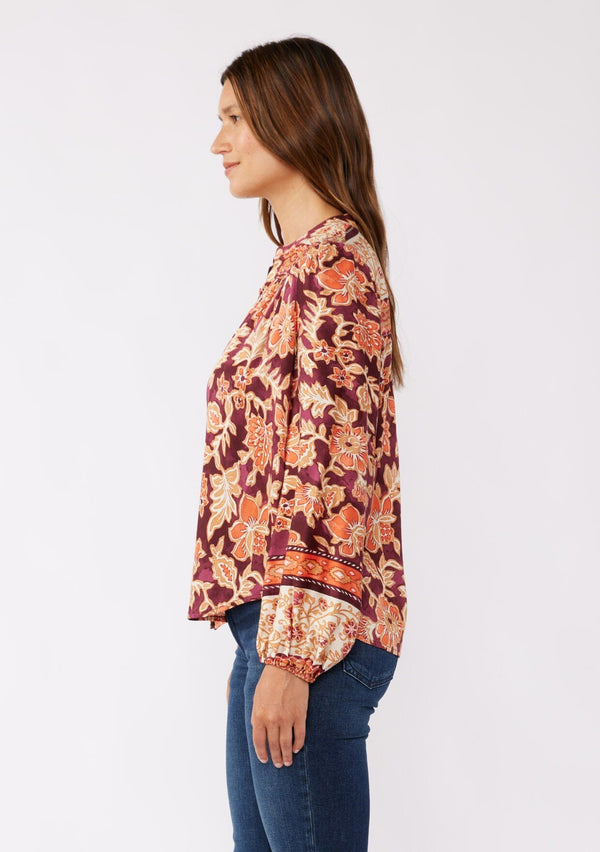 [Color: Wine/Dusty Rose] A side mage of a brunette model wearing an orange and red floral print blouse with a functional button front. With a relaxed fit, split v neckline, long sleeves, and elastic cuffs. 