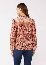 [Color: Wine/Dusty Rose] A back mage of a brunette model wearing an orange and red floral print blouse with a functional button front. With a relaxed fit, split v neckline, long sleeves, and elastic cuffs. 