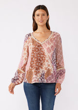 [Color: Natural/Clay] A front image of brunette model wearing a bohemian long sleeve blouse with a pink patchwork print. A relaxed fit style with a classic v neckline, elastic cuffs, pintuck details, and unique burlap trim inserts. Perfectly styled with dark denim for a laid back fall vibe. 