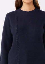 [Color: Navy] A brunette model wearing a classic crew neck sweater in navy blue. With ribbed trims, long sleeves, and a cable knit stitch detail. A versatile sweater perfect for layering during colder temperatures or wearing on its own. 