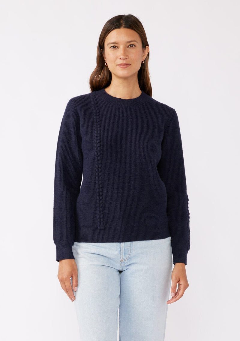 [Color: Navy] A brunette model wearing a classic crew neck sweater in navy blue. With ribbed trims, long sleeves, and a cable knit stitch detail. A versatile sweater perfect for layering during colder temperatures or wearing on its own. 