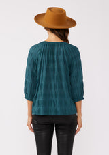 [Color: Deep Teal] A back facing image of a brunette model wearing a textured jacquard stripe blouse in teal. A relaxed fit blouse with a split v neckline and long sleeves. Styled with dark denim for the fall season. 