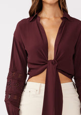 [Color: Merlot] A detailed image of a brunette model wearing a sexy wine burgundy tie front top with embroidered and lace trim details. A casual, everyday black top with a collared neckline, long sleeves, and an elastic wrist cuff. Perfect for elevating any fall wardrobe. 