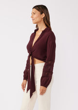 [Color: Merlot] A side image of a brunette model wearing a sexy wine burgundy tie front top with embroidered and lace trim details. A casual, everyday black top with a collared neckline, long sleeves, and an elastic wrist cuff. Perfect for elevating any fall wardrobe. 