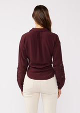 [Color: Merlot] A back image of a brunette model wearing a sexy wine burgundy tie front top with embroidered and lace trim details. A casual, everyday black top with a collared neckline, long sleeves, and an elastic wrist cuff. Perfect for elevating any fall wardrobe. 