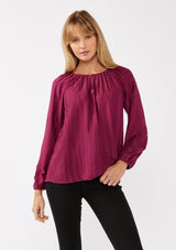 [Color: Wine] A  front facing image of a blonde model wearing a bohemian pink blouse with embroidered details. With long raglan sleeves, a round neckline with a single button closure, a front keyhole, and a relaxed fit.