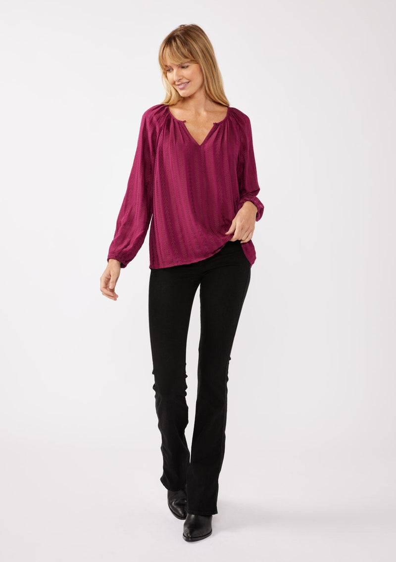 [Color: Wine] A full body front facing image of a blonde model wearing a bohemian pink blouse with embroidered details. With long raglan sleeves, a round neckline with a single button closure, a front keyhole, and a relaxed fit.