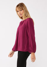 [Color: Wine] A side facing image of a blonde model wearing a bohemian pink blouse with embroidered details. With long raglan sleeves, a round neckline with a single button closure, a front keyhole, and a relaxed fit.