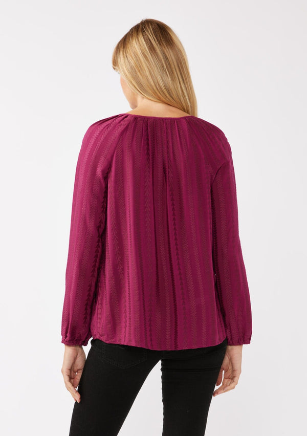 [Color: Wine] A back facing image of a blonde model wearing a bohemian pink blouse with embroidered details. With long raglan sleeves, a round neckline with a single button closure, a front keyhole, and a relaxed fit.