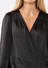 [Color: Black] A detail image of a blonde model wearing a holiday black silky polyester satin top. This special occasion top features a surplice v neckline, front hook and eye closure, elastic hemline, and long sleeves. Perfect for Christmas and holiday parties. 